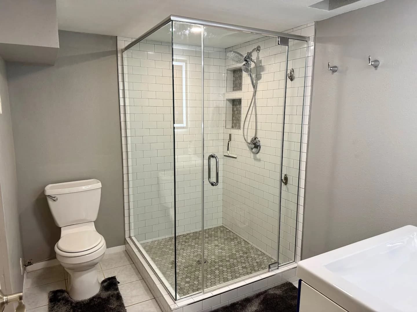 Downstairs bathroom with a glass-enclosed shower, raised tile threshold, white subway tile, and a toilet beside it