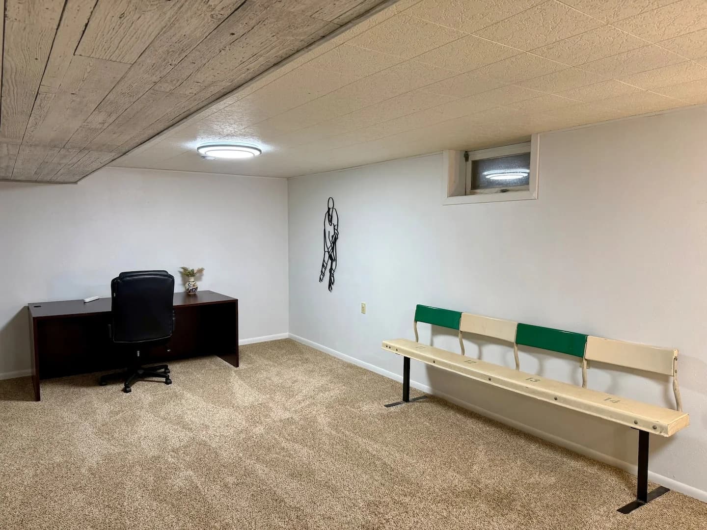 Green and cream arena bench along the downstairs wall beside a wooden desk and black office chair