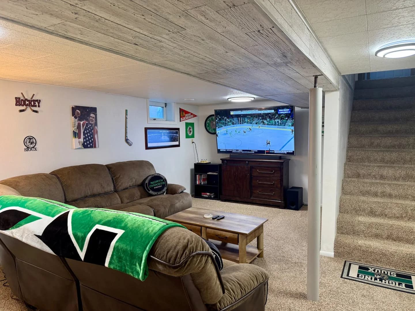Large TV showing hockey beside the sectional, with framed hockey photos, a pennant, and a hockey stick on the wall