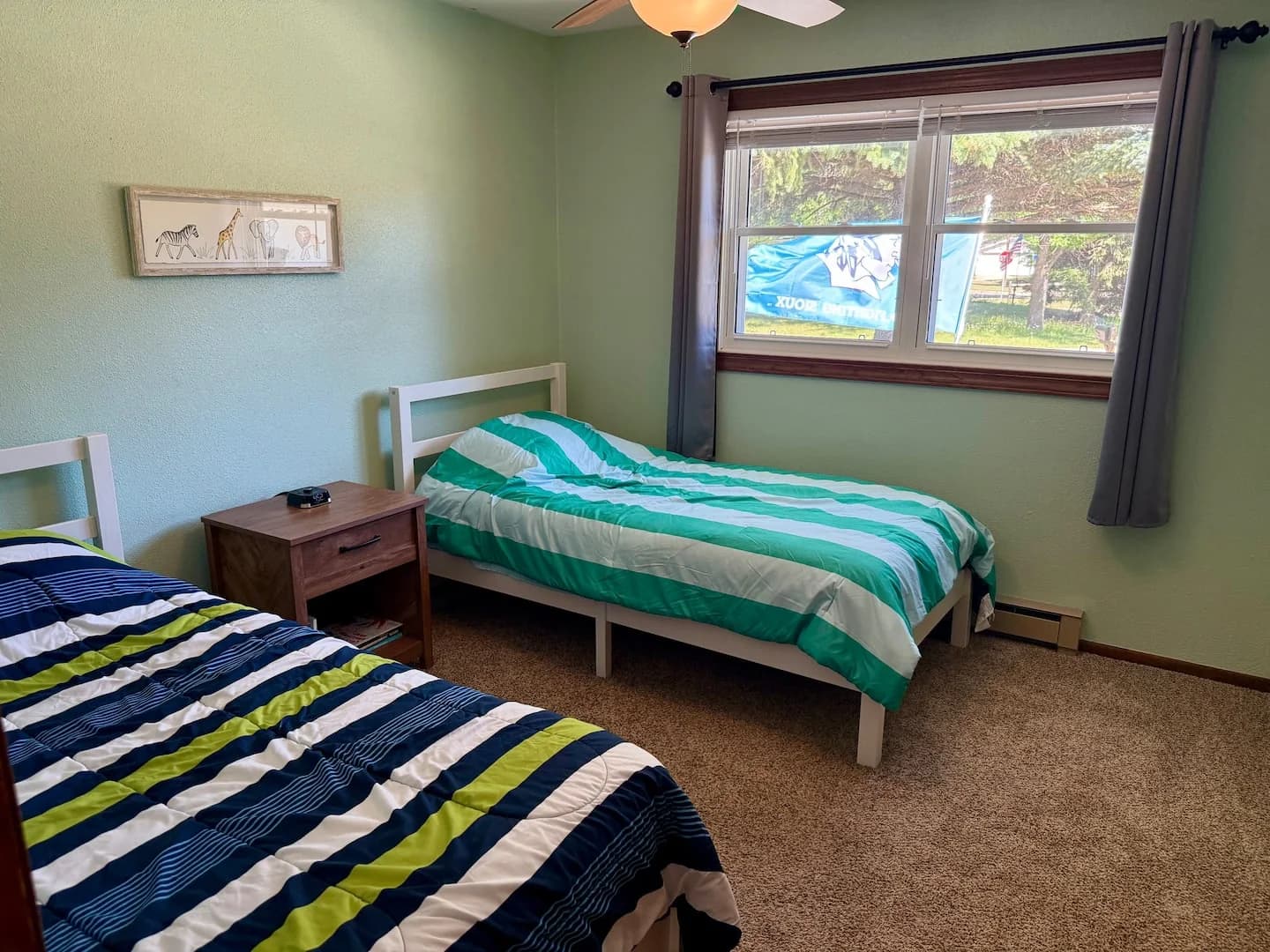 Two twin beds with striped bedding and a shared nightstand beneath a wide window